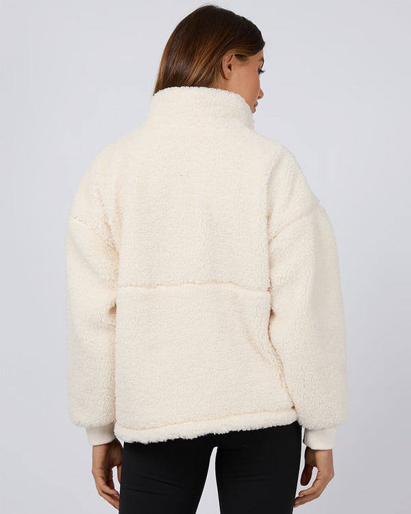 Back view of a cream sherpa fleece pullover with a high collar and relaxed fit, worn by a model in black leggings.