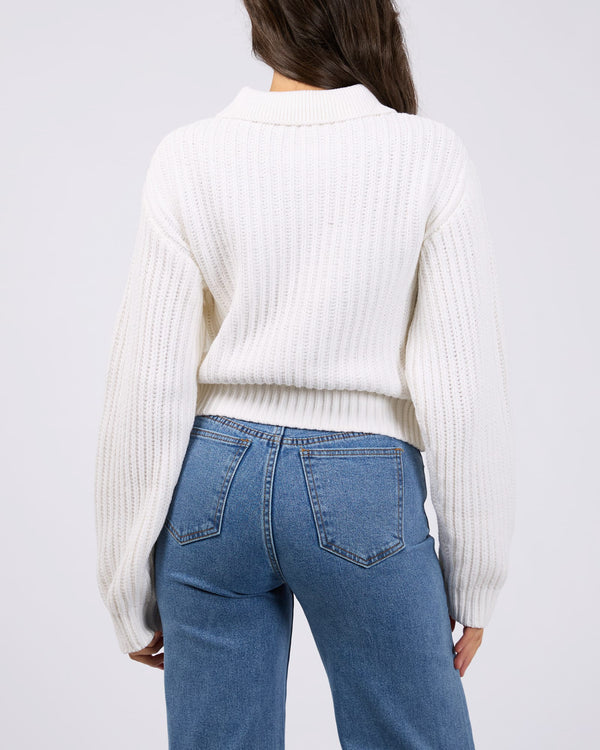 Back view of a model wearing a white ribbed knit cardigan with a collar and balloon sleeves, paired with blue jeans.