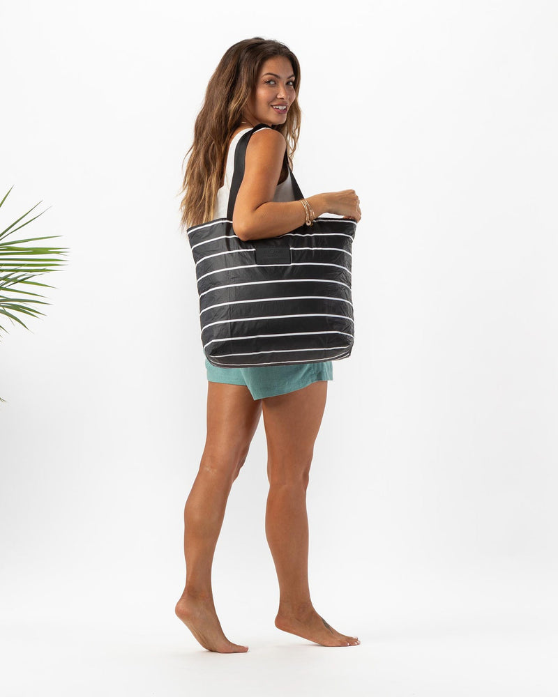Woman carrying black striped tote bag with a relaxed summer outfit and bare feet