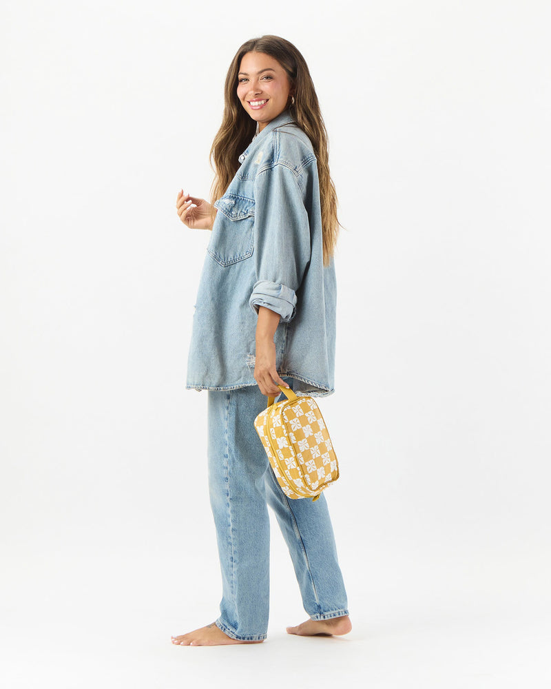 Smiling woman in denim outfit holding yellow floral pouch by ALOHA Collection