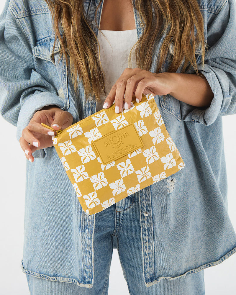 Woman holding yellow floral ALOHA pouch styled with a white top and denim jacket