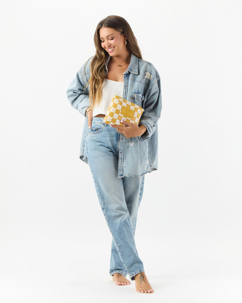 Full body view of woman holding yellow floral ALOHA pouch with relaxed denim outfit