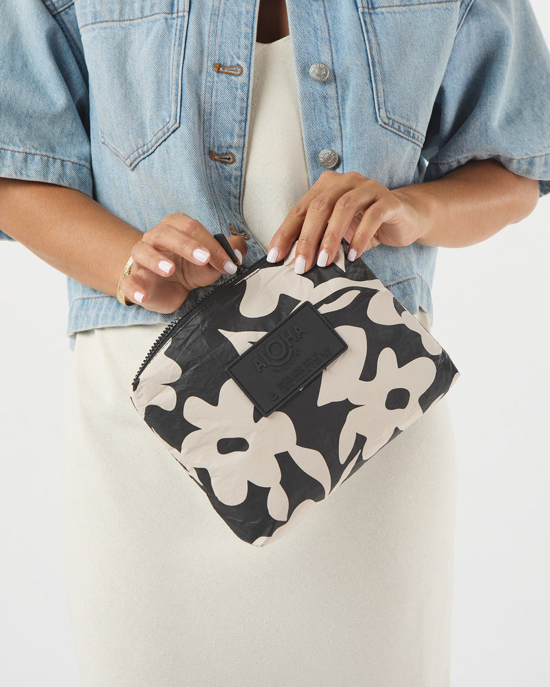 Woman holding floral ALOHA pouch with zip closure, styled with a white dress and denim jacket