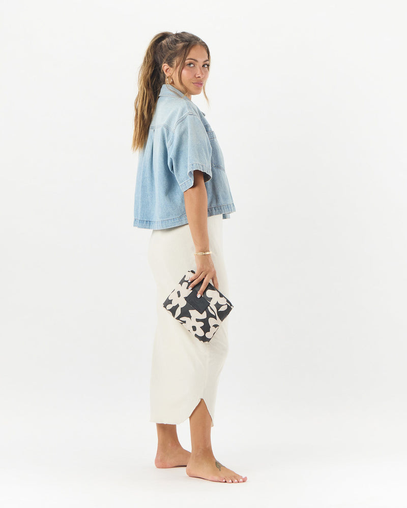 Side view of woman holding floral ALOHA pouch styled with a white skirt and cropped denim jacket
