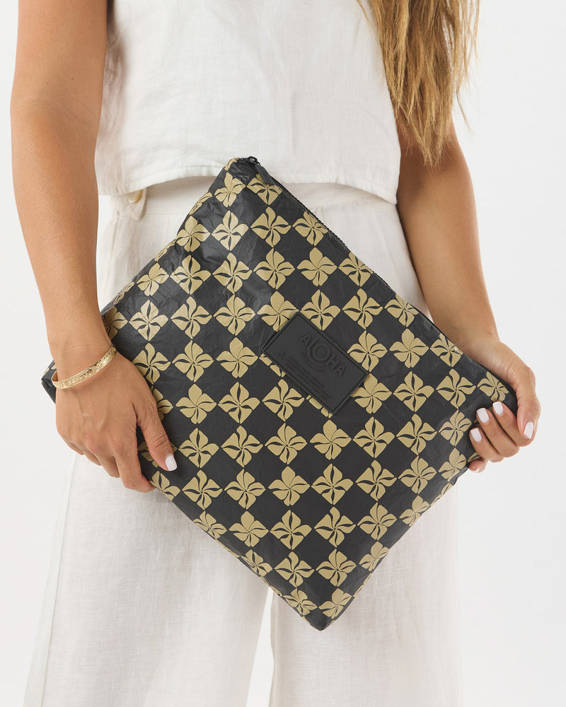 ALOHA pouch held underarm, showing versatile size and bold floral checkerboard pattern