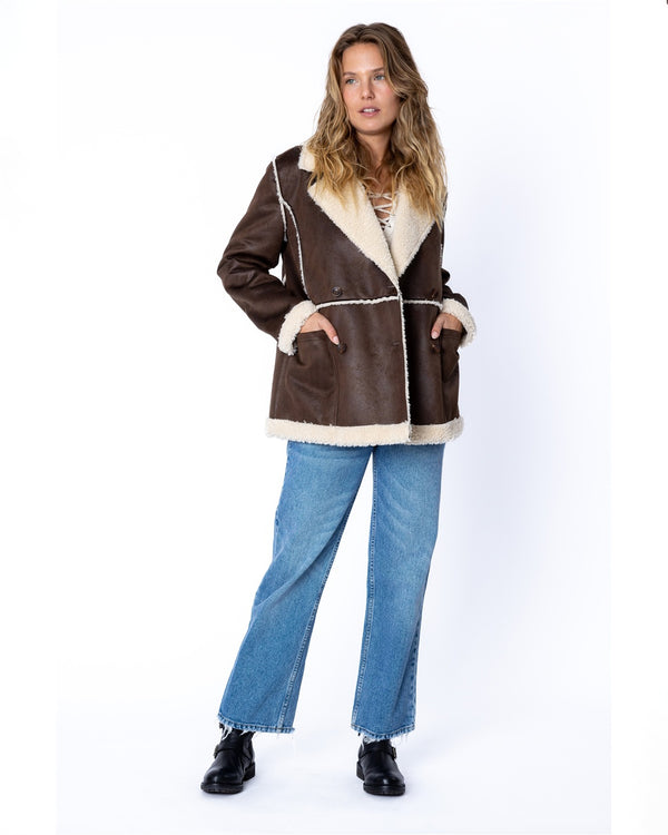 Women's brown faux shearling jacket with white contrast stitching, wide lapels, and cozy cream lining.