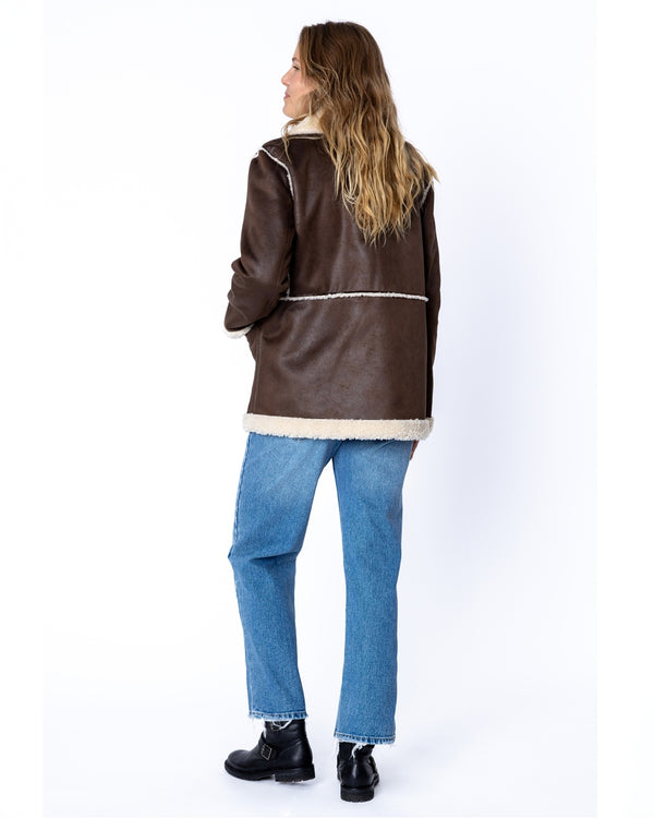 Back view of a women's brown faux shearling jacket with white contrast stitching and cream lining on hem and collar.