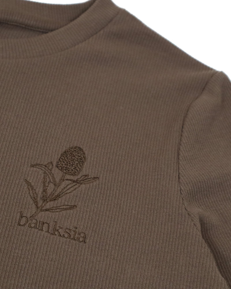 Close-up of embroidered Banksia flower and text on ribbed brown fabric