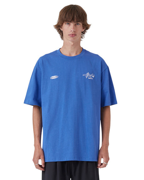 Oversized blue graphic tee with chest prints, styled with black shorts.