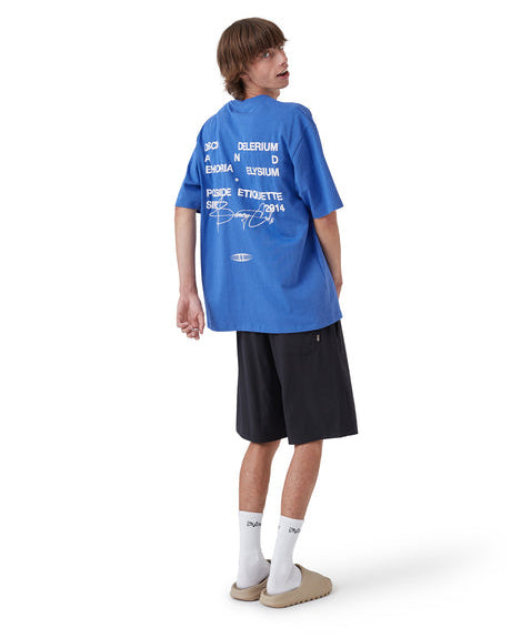 Back of graphic tee featuring large white print, paired with black shorts and beige slides.