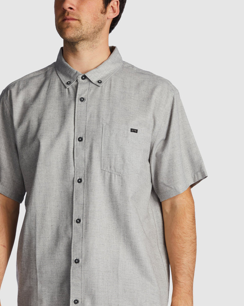 Close-up of grey shirt showing chest pocket and small black logo patch.