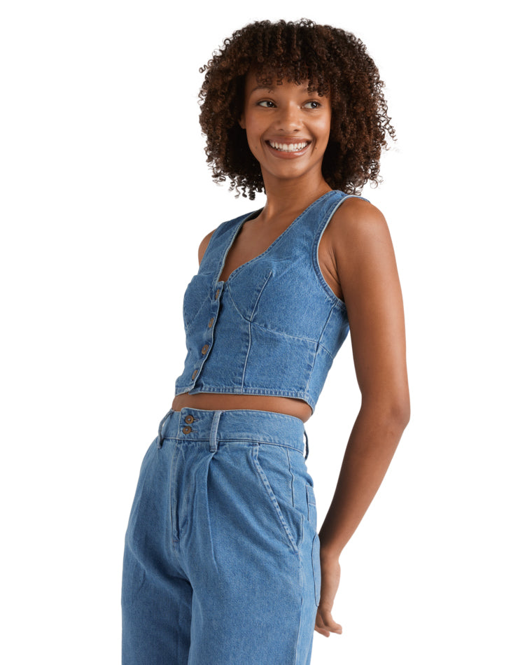 Side angle of a denim crop vest with button details, styled with pleated wide-leg jeans.