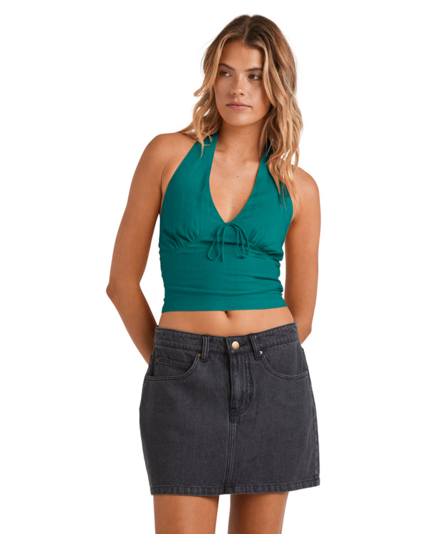 Woman wearing a teal halter neck crop top with a tie detail and a black denim mini skirt.