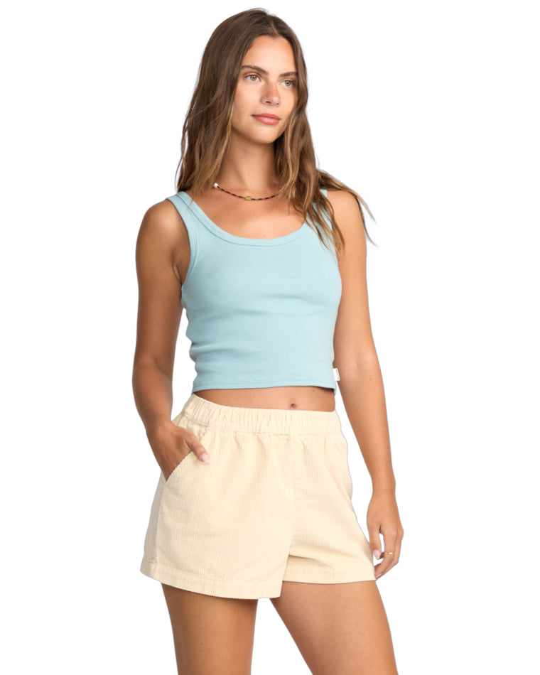 Side view of light blue tank and cream cord shorts with model's hand in pocket