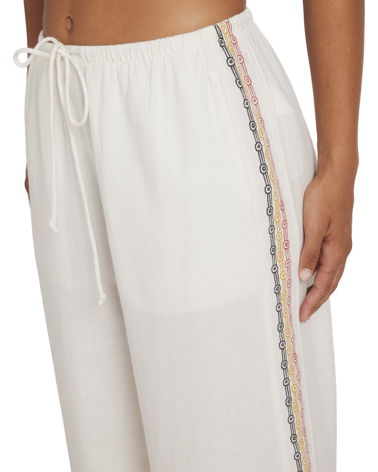 Close-up of white pants showing multicolour side embroidery and drawstring waistband detail.