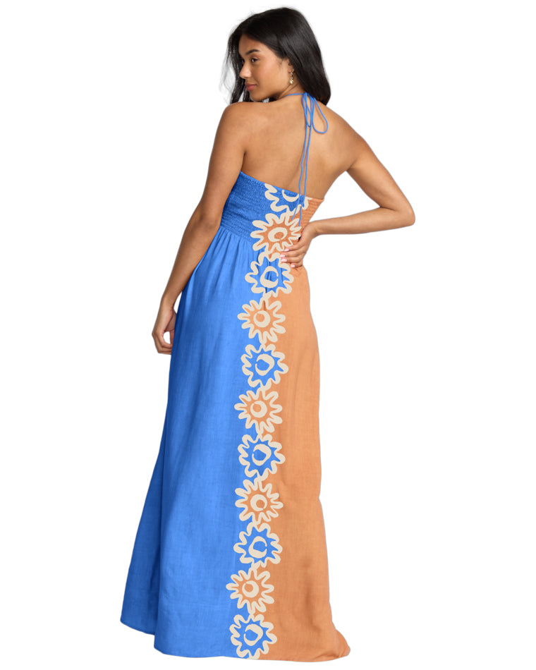 Back view of a halterneck maxi dress with blue shirred bodice and floral panel down the centre back.
