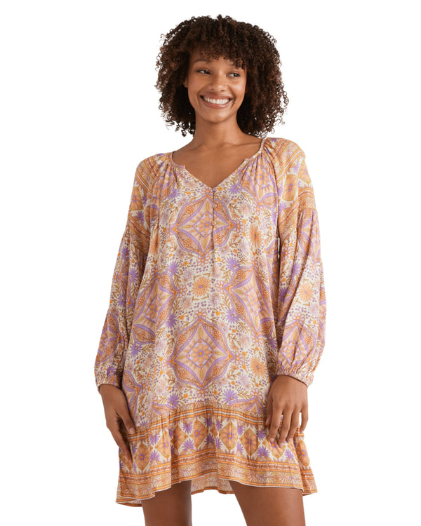 Woman wearing a long-sleeve mini dress with an orange, purple and white boho-style floral print.