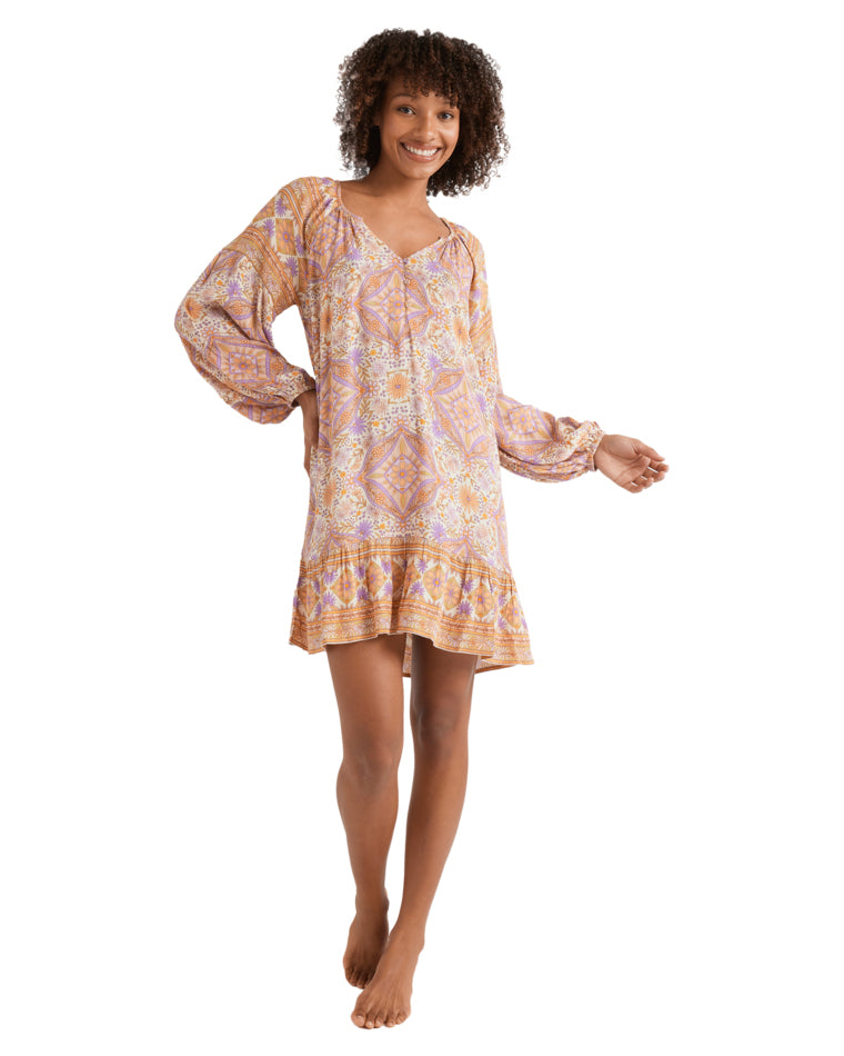 Full-length view of the woman in the printed long-sleeve mini dress, standing barefoot.