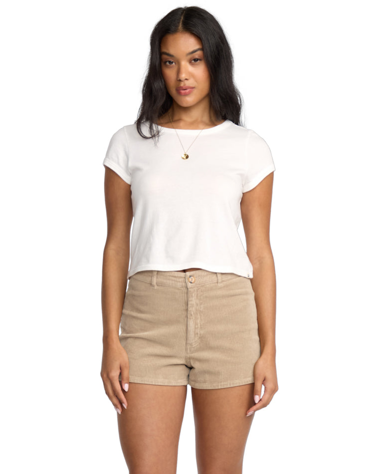 Model wears a white cropped tee and high-waisted beige corduroy shorts, standing front on.