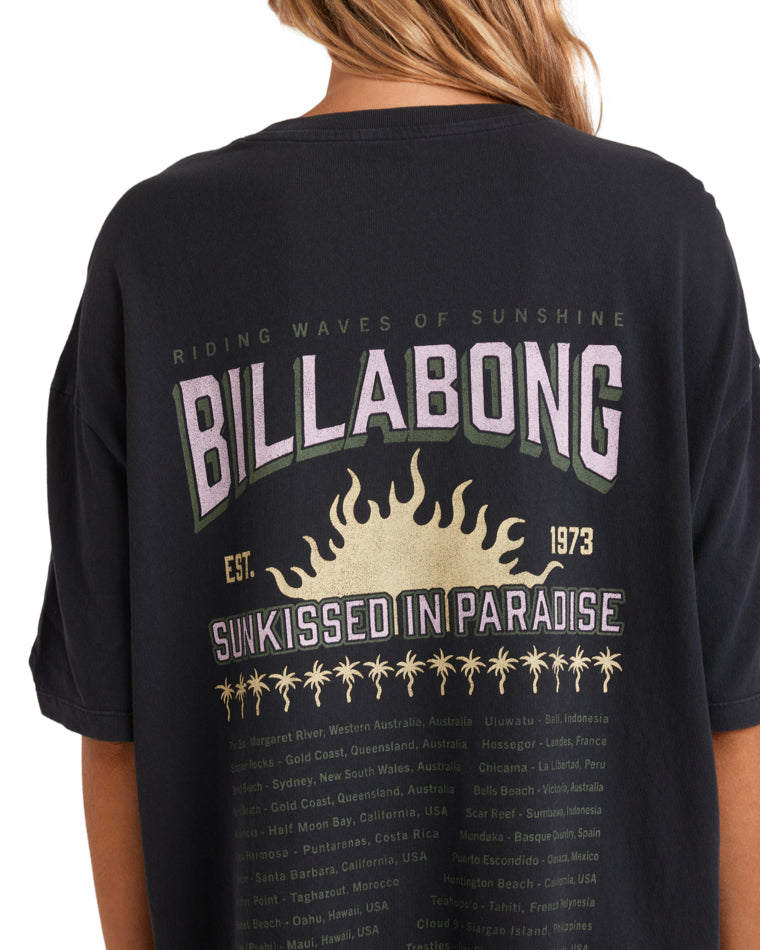 Close-up of the back print on a black Billabong t-shirt with purple text, sun illustration, and beach locations listed.