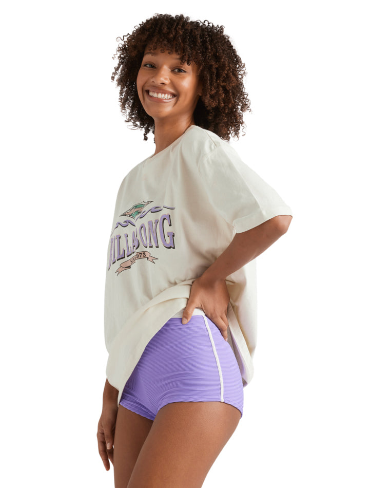 Side view of woman smiling in oversized Billabong tee and ribbed shorts with white trim.