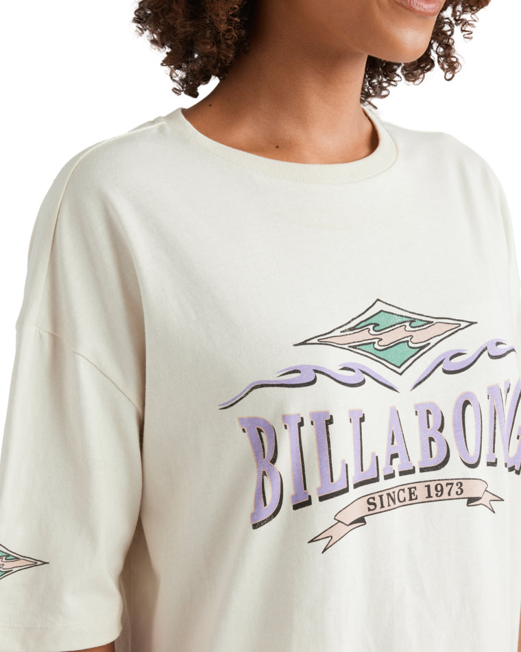 Close-up of Billabong logo print on cream oversized tee with pastel graphics.