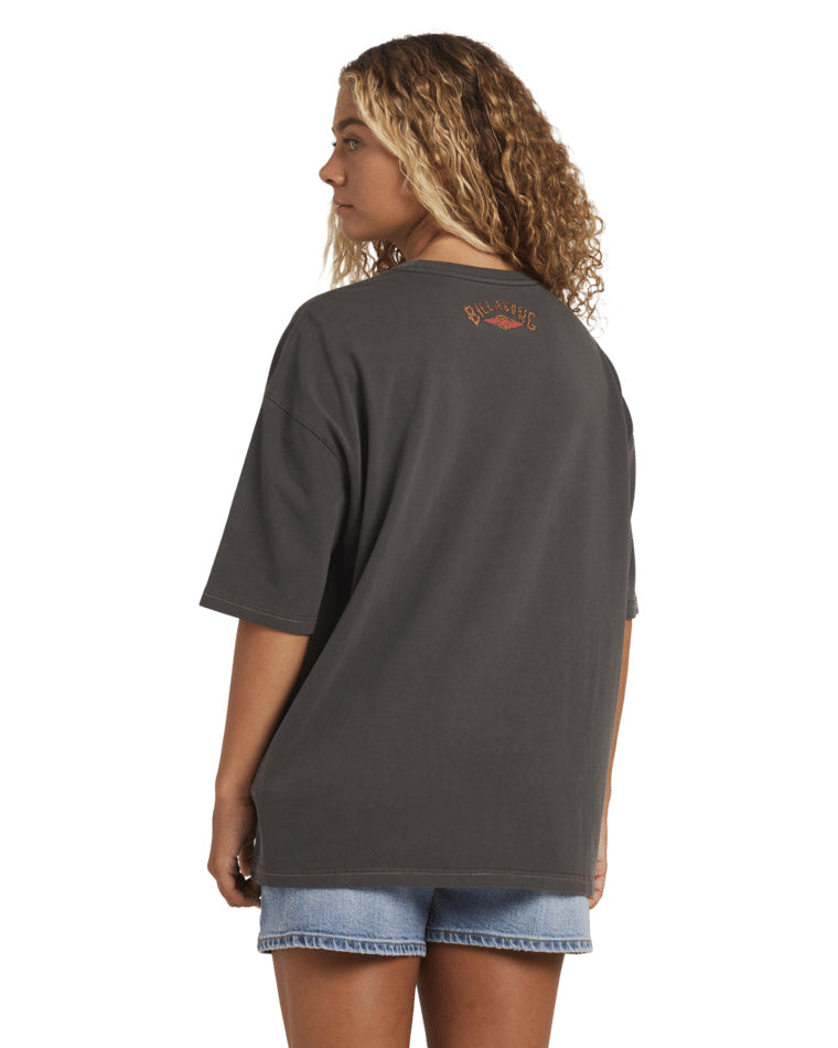Back view of a black Billabong t-shirt with orange logo print near the neckline, styled with blue denim shorts.