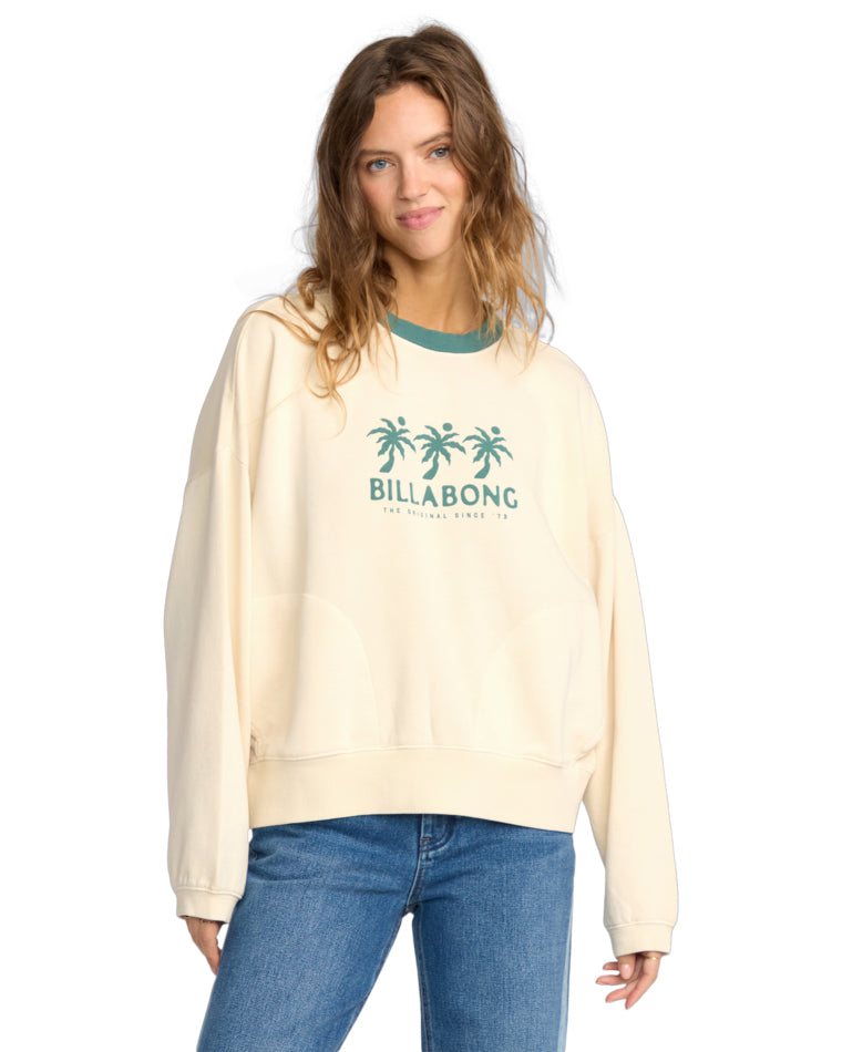 Cream crew neck sweatshirt with teal palm tree and Billabong logo on front, worn with jeans.