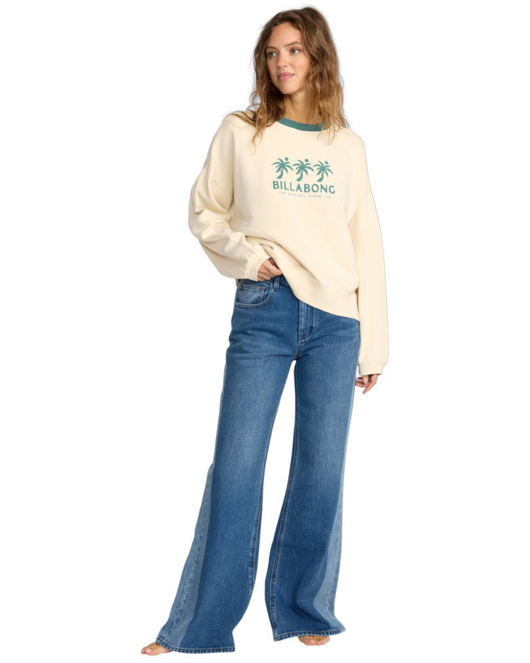 Full-length view of a model wearing a cream Billabong sweatshirt and high-waisted wide-leg jeans.