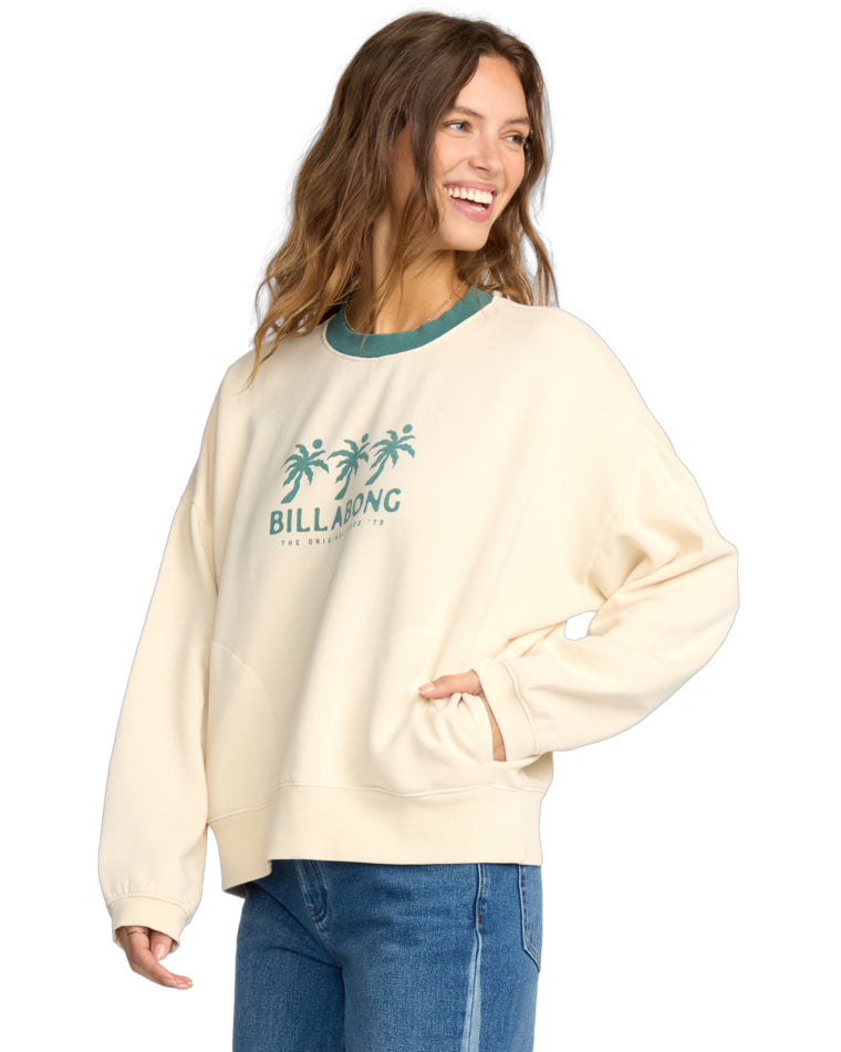 Relaxed-fit cream sweatshirt with green neckline and Billabong print, paired with blue flared jeans.