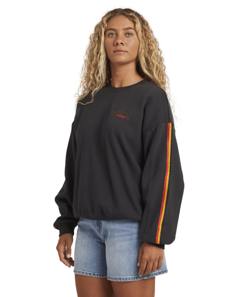 Side view of black crewneck with red and yellow sleeve stripe and small front chest logo, styled with shorts