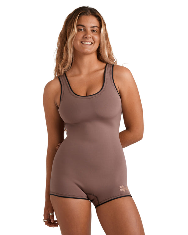Woman wearing a sleeveless brown wetsuit with black seams and a scoop neckline, standing front-on.