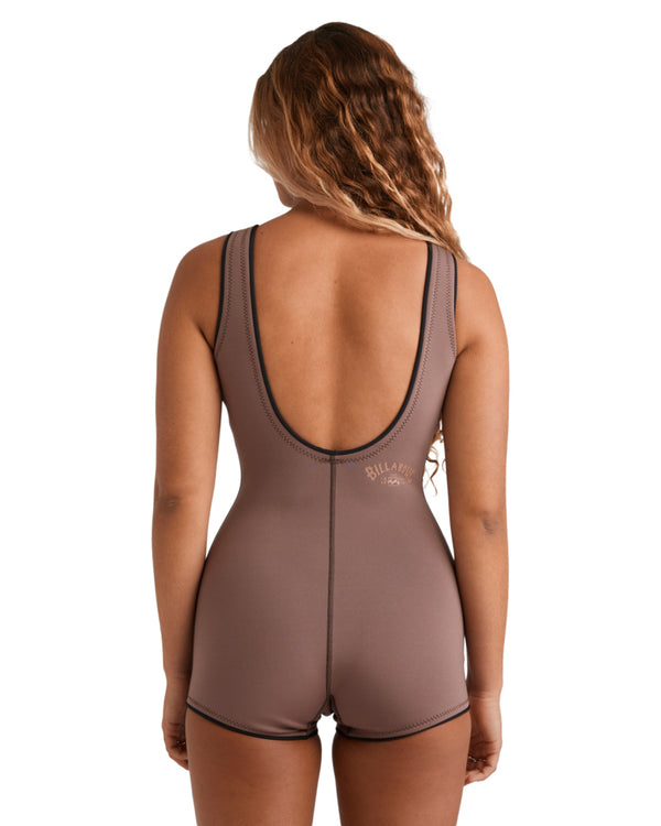 Woman wearing a sleeveless brown wetsuit with black trim, standing front-on with arms behind her back.