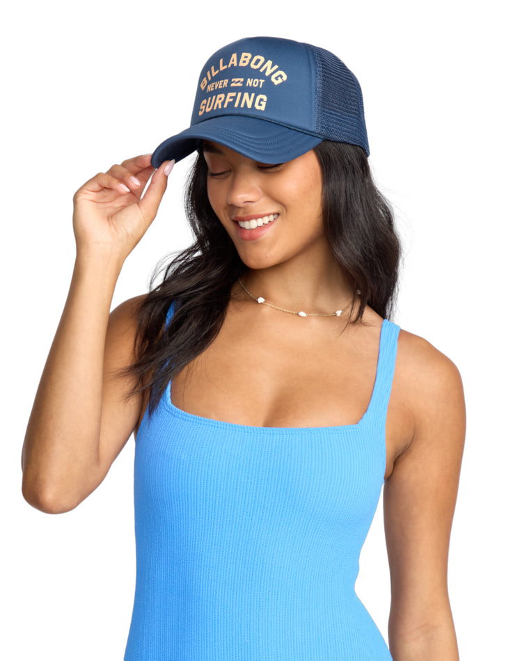 Model wearing blue Billabong trucker cap with “Never Not Surfing” slogan.