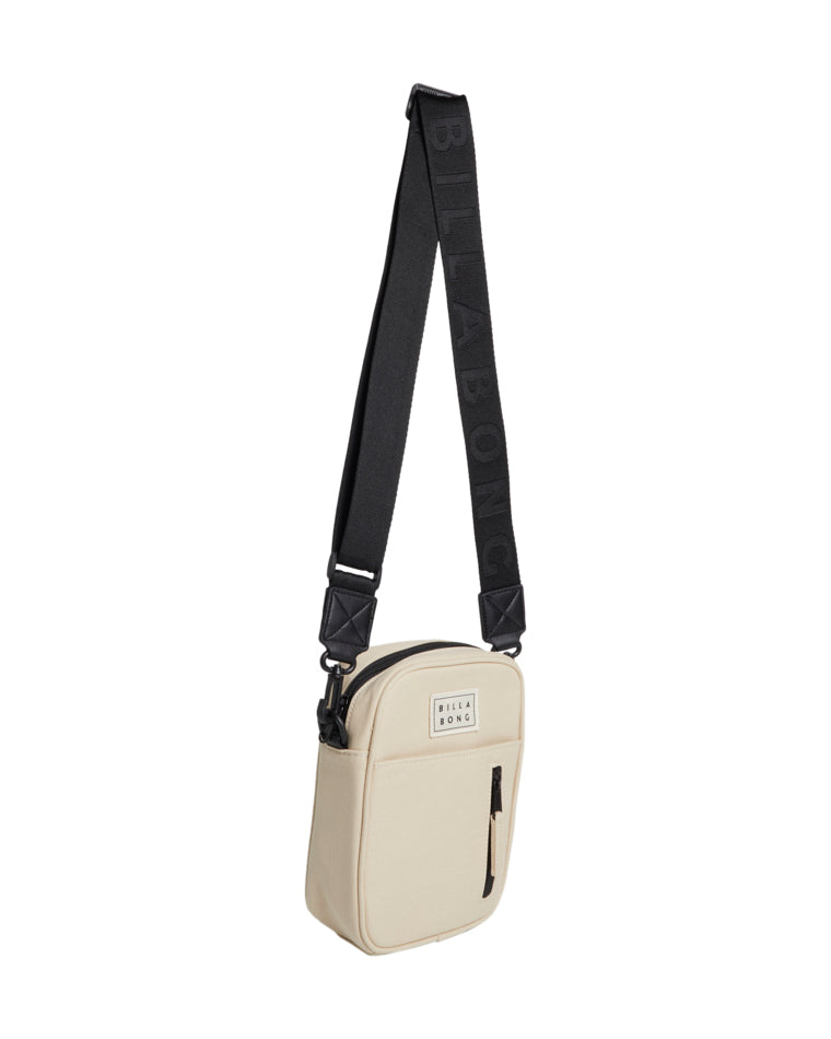 Side angle of beige Billabong crossbody bag with front zip pocket and thick black shoulder strap.