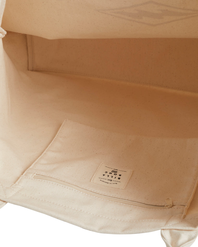 Inside view of cream tote bag featuring an internal pocket with zipper and logo patch.