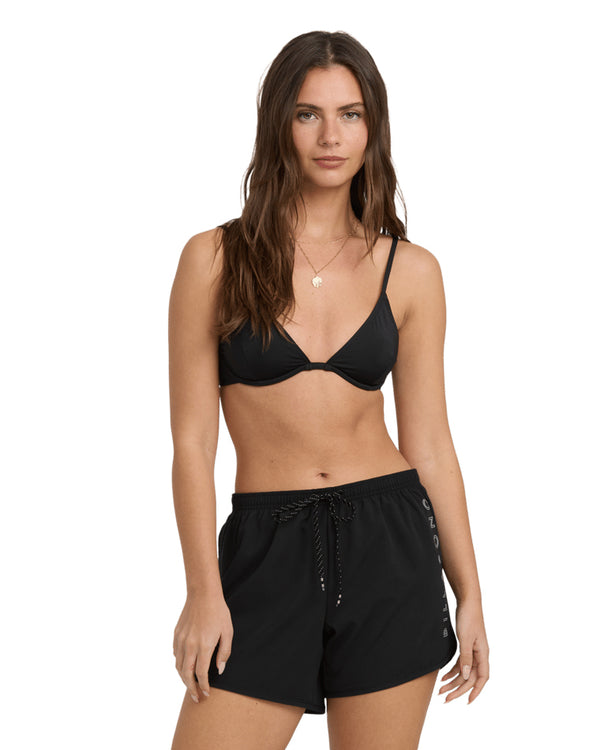 Woman wearing a black bikini top and black Billabong logo shorts with drawstring waist.