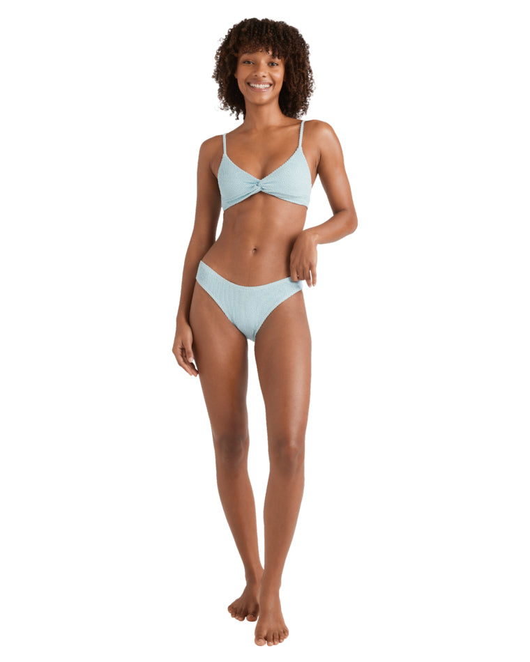 Front-facing view of a woman smiling in a textured light blue bikini top with thin straps and twist front.