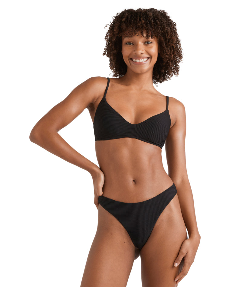Woman wearing a textured black bikini with adjustable straps and a deep V neckline, smiling with hand on hip.