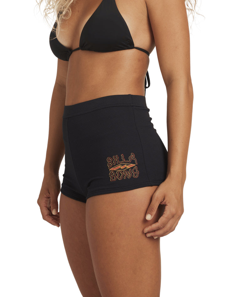 Rear side view of woman in black bikini and high-waisted swim shorts, showing the curve of the waistband.