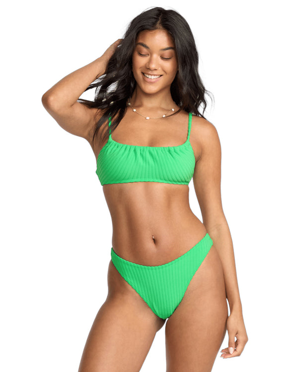 Woman wearing a green textured bikini, smiling with one hand in her hair.