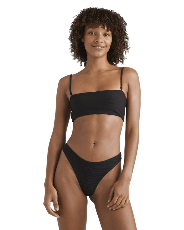 Woman wearing a black bandeau bikini set with thin straps, smiling and standing front-on.