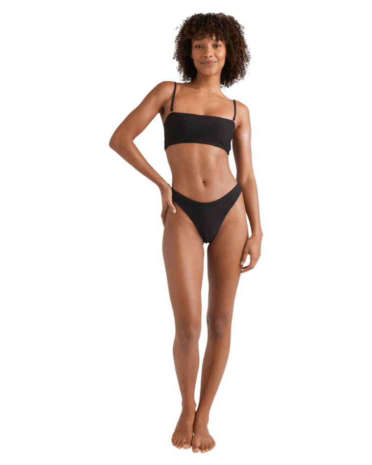 Full body shot of woman in a black bandeau bikini, standing with one hand on hip and smiling.