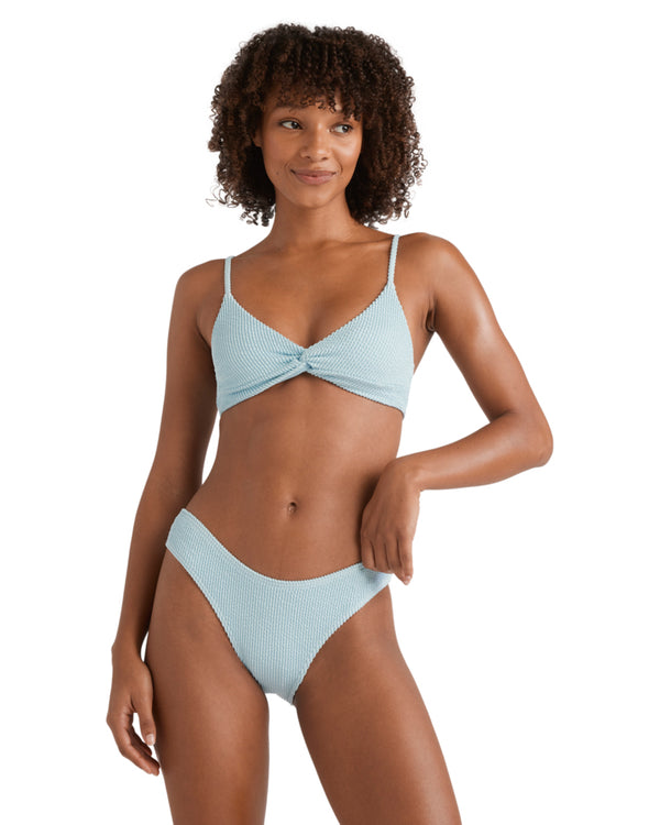 Woman wearing a pale blue textured bikini set with a twist-front bralette top and high-cut bottoms.