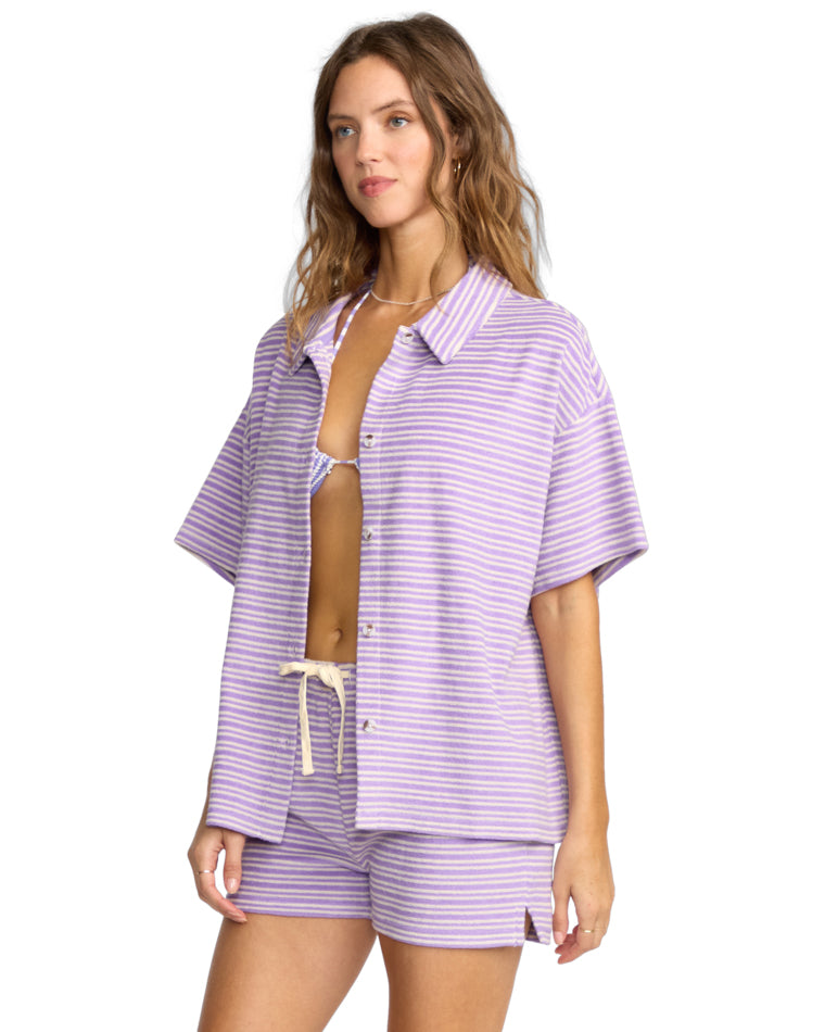 Side view of woman in lavender and white striped short-sleeve set, one hand at side.
