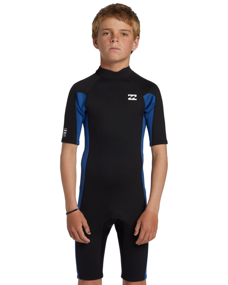 Boy wearing a black and blue Billabong short sleeve wetsuit, front view with logo on chest.