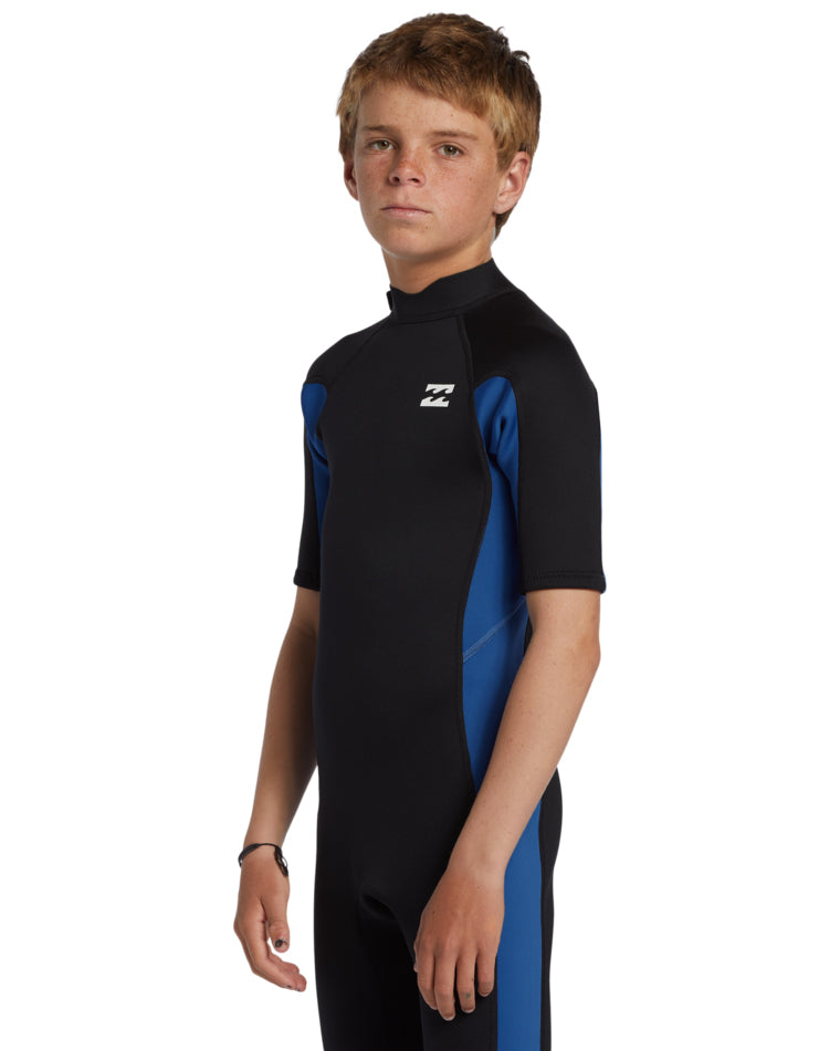 Boy in side profile wearing black and blue Billabong wetsuit with contrast sleeve panels.