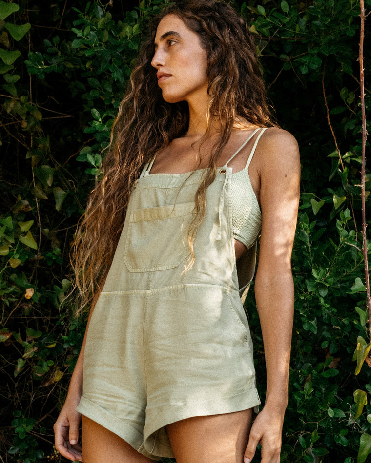 Woman wearing olive green short overalls over a textured crop top.
