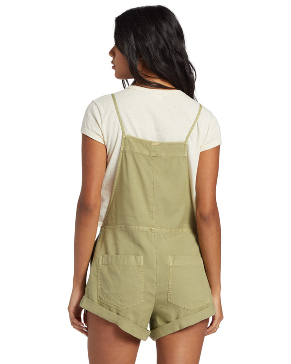 Back view of olive green short overalls featuring back patch pockets and slim straps over a white tee.