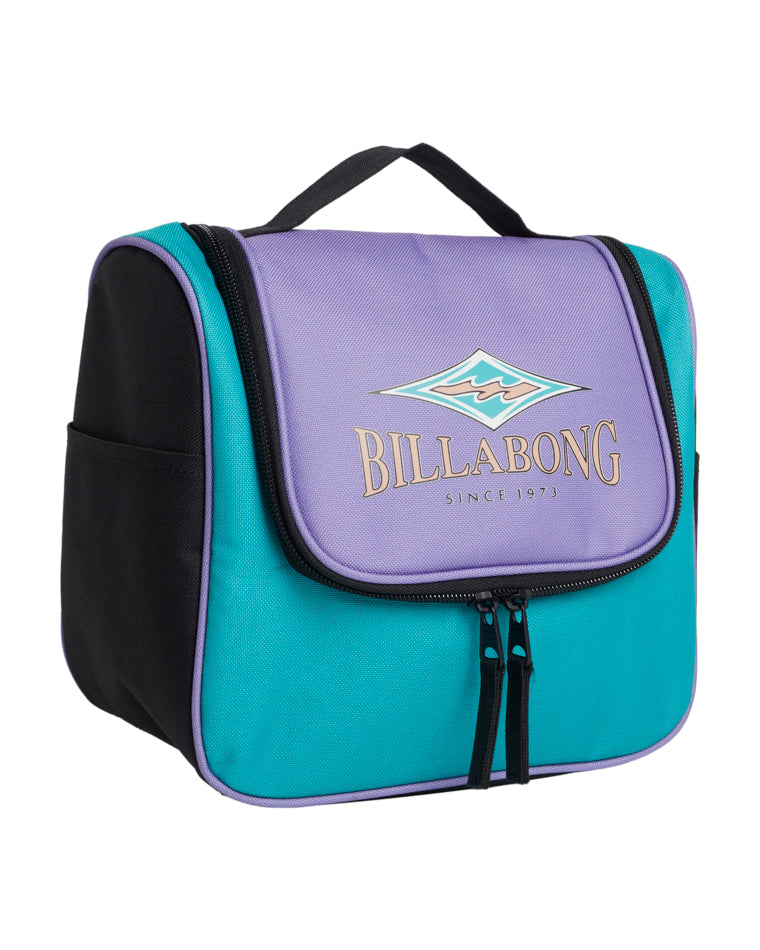 Angled front-side view of a Billabong travel bag with a purple flap, teal body, black side panels, dual zipper pulls, and logo reading “Since 1973.”
